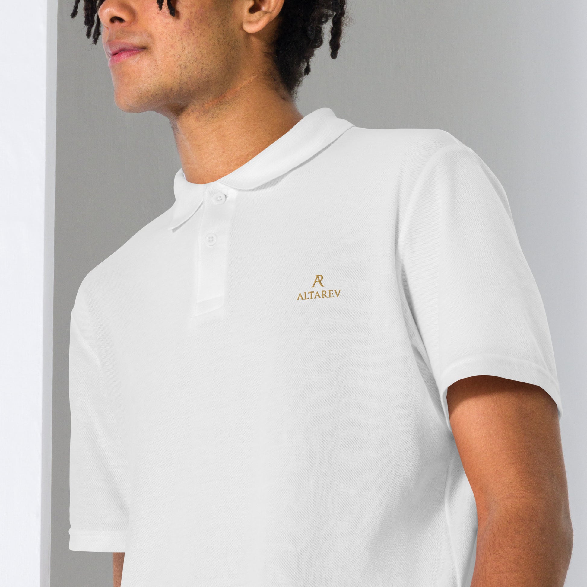 Gros plan sur un polo blanc ALTAREV avec broderie dorée élégante du logo AR sur la poitrine gauche.

